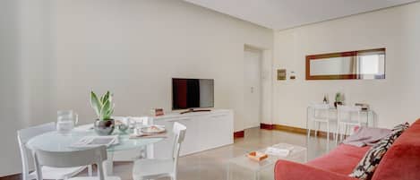 Ein modernes Wohnzimmer mit einem Glastisch, weißen Stühlen, einem roten Sofa und einem Flachbildfernseher auf einer weißen Kommode.