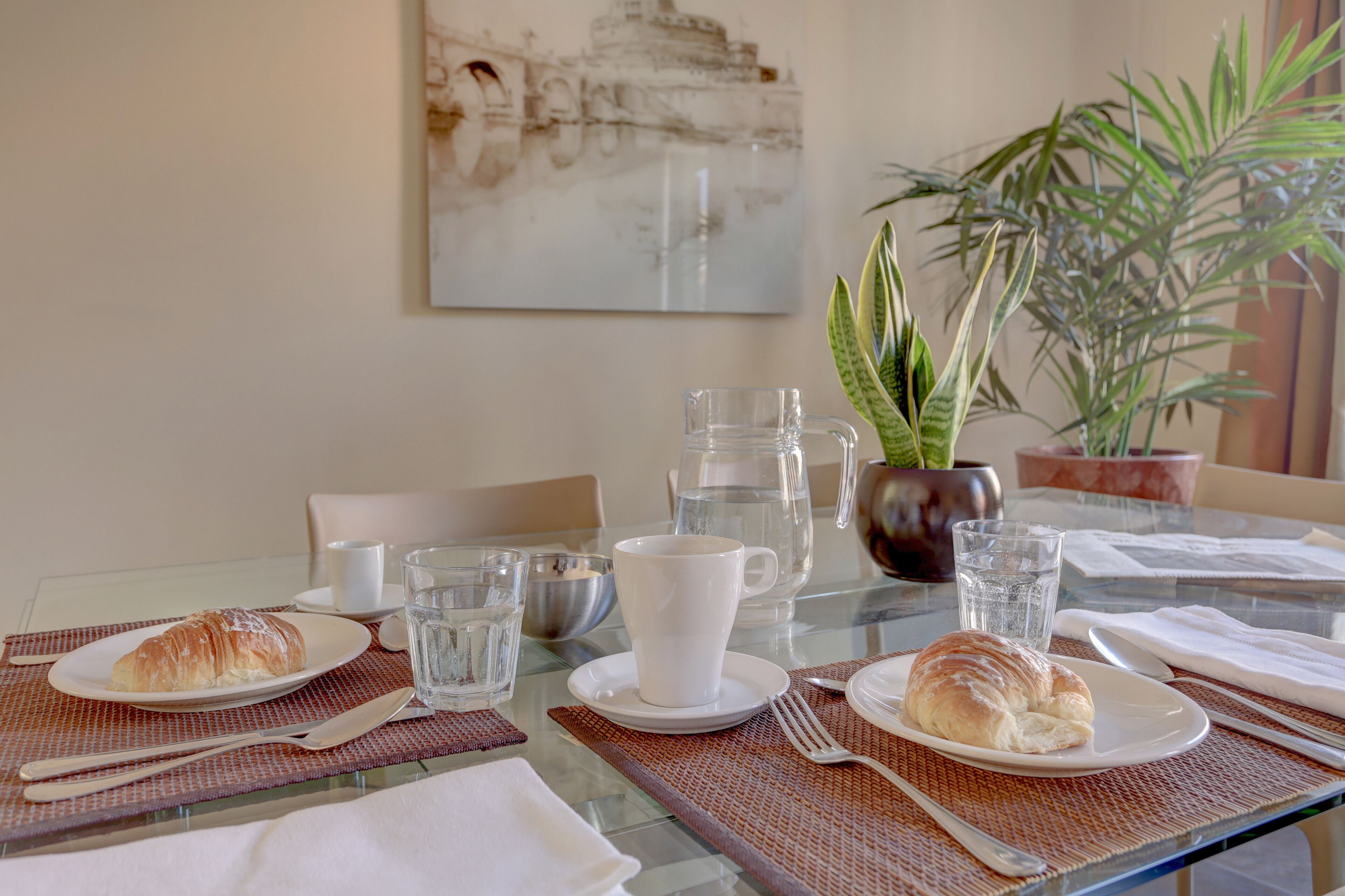 Une table à manger dressée avec des croissants, une tasse blanche et des verres à eau.