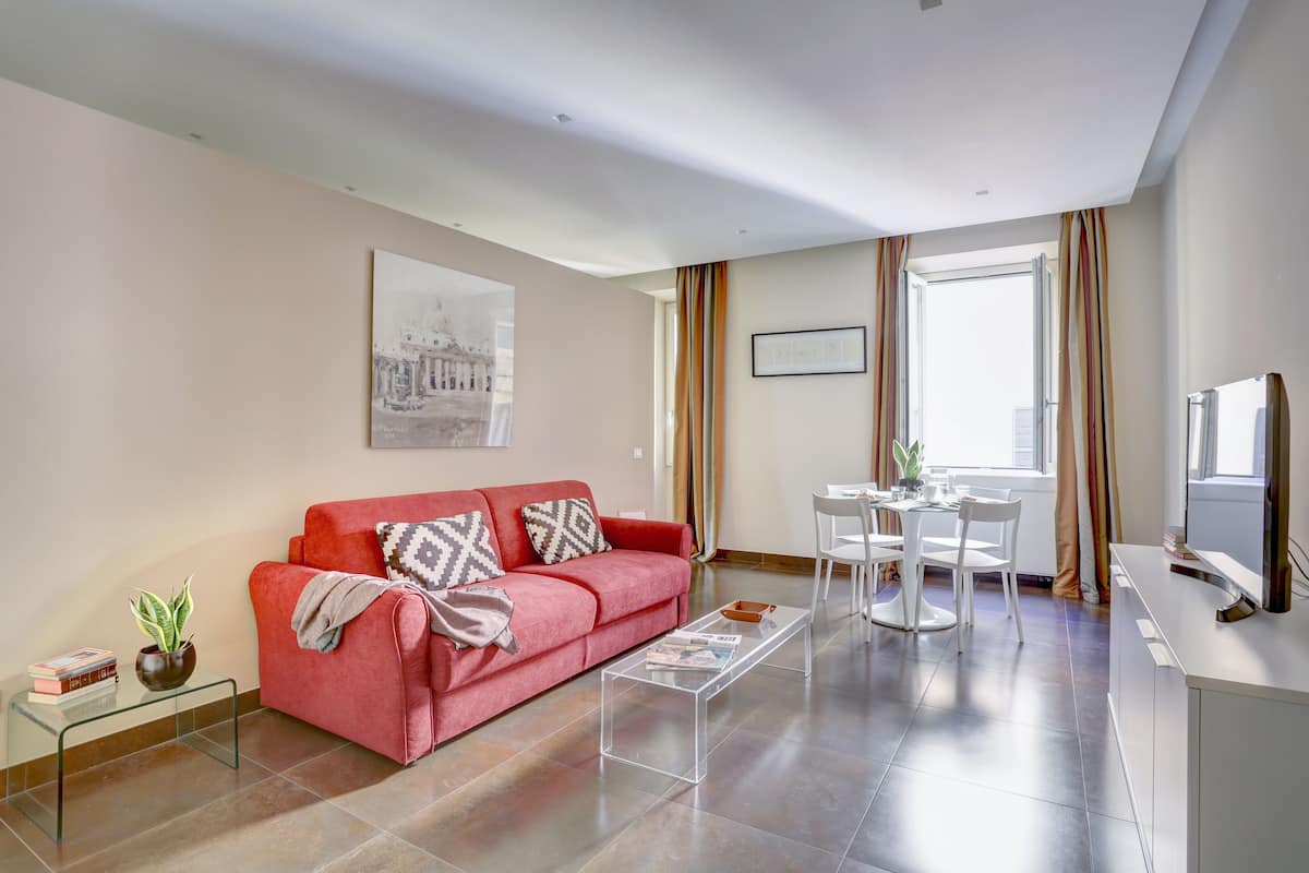 A modern living room with a red sofa, a glass coffee table, and a dining area with a white table and chairs.