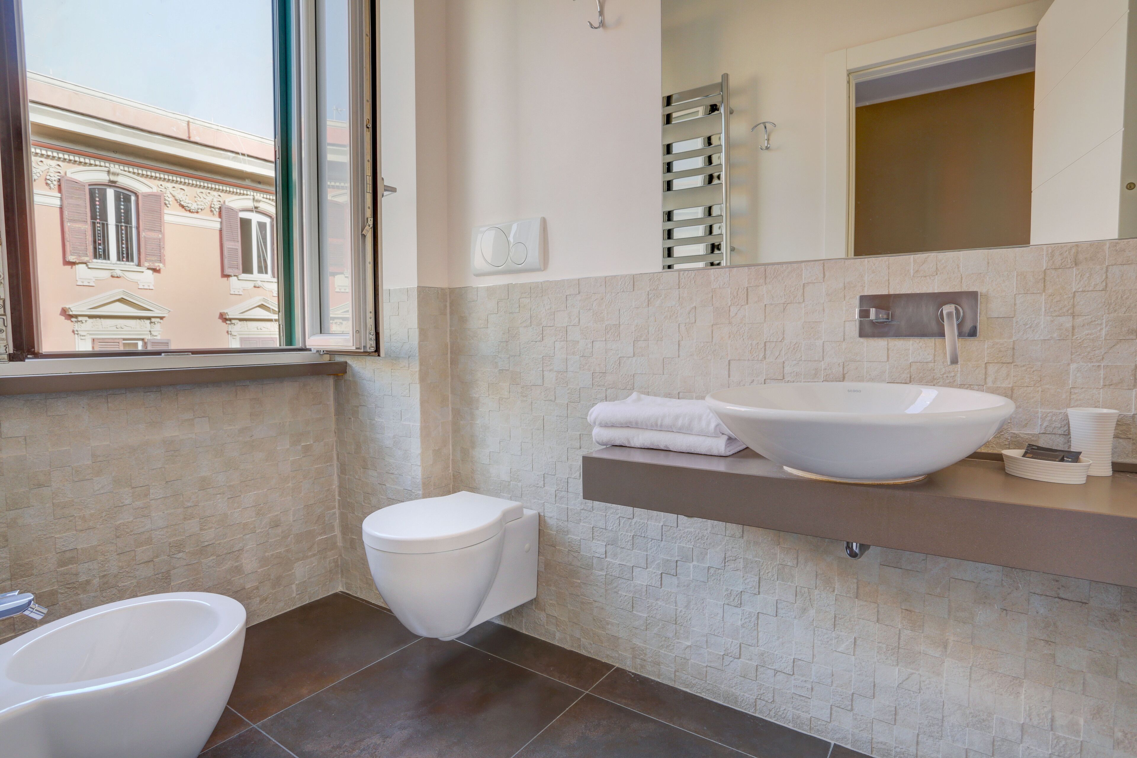 A modern bathroom with a large window, a white toilet, a white sink, and a towel rack.