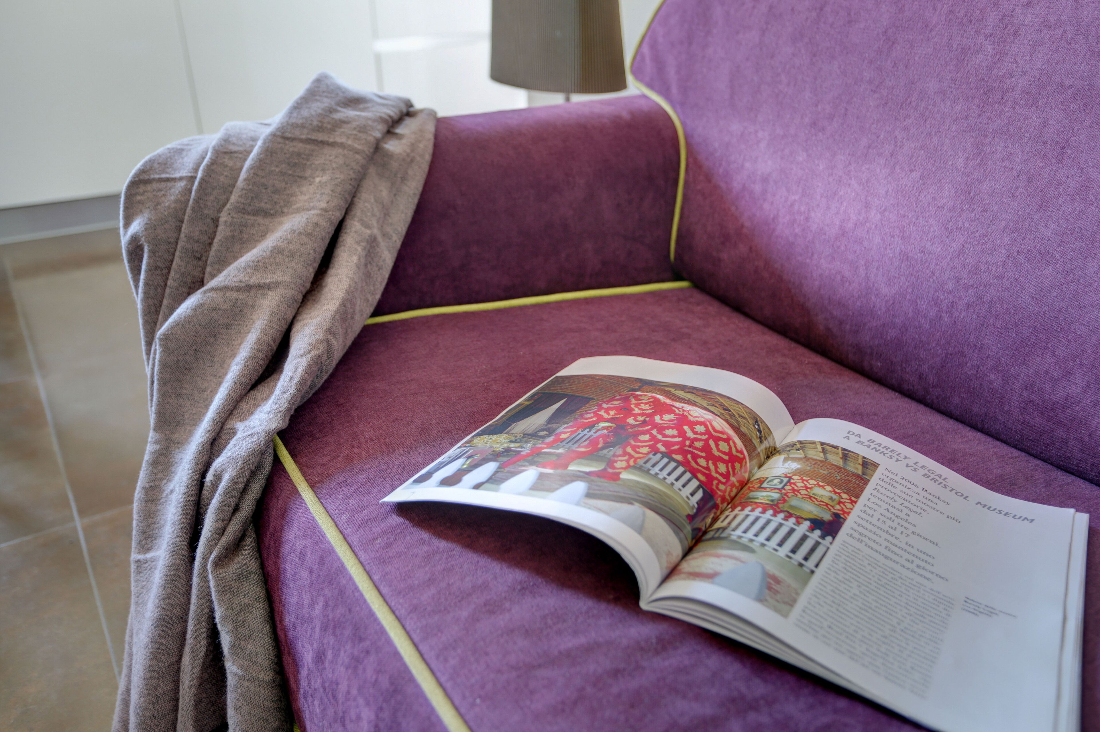 A magazine on a purple sofa with a blanket draped over it.