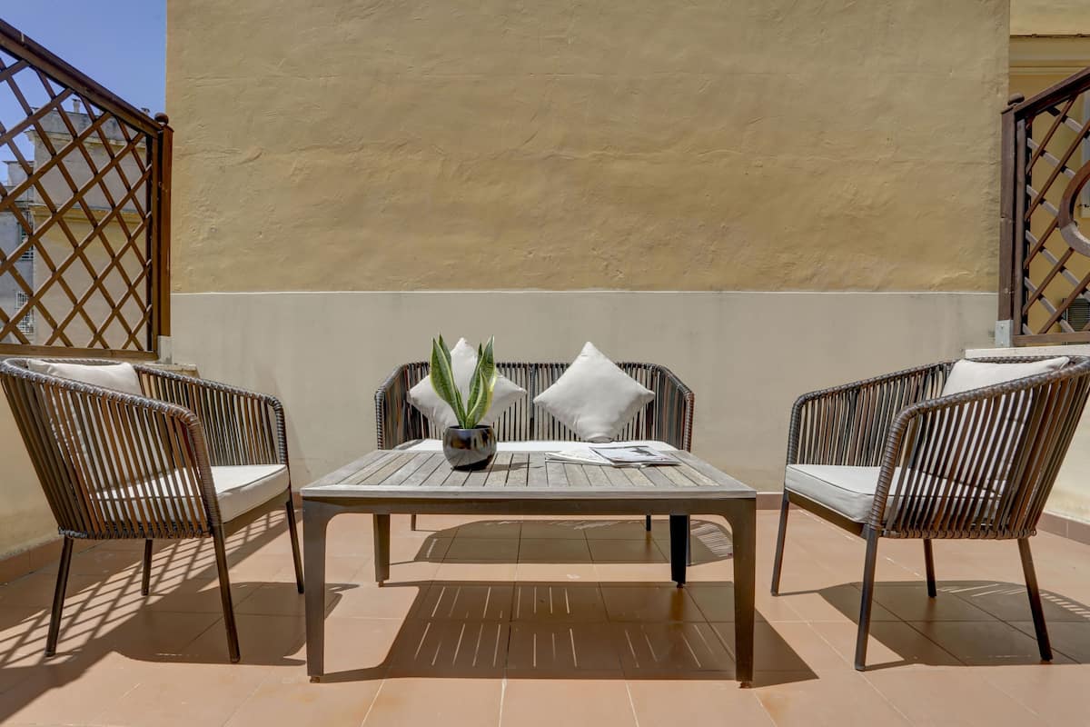 A patio with a table and two wicker chairs, a potted plant, and a white cushion on the table.