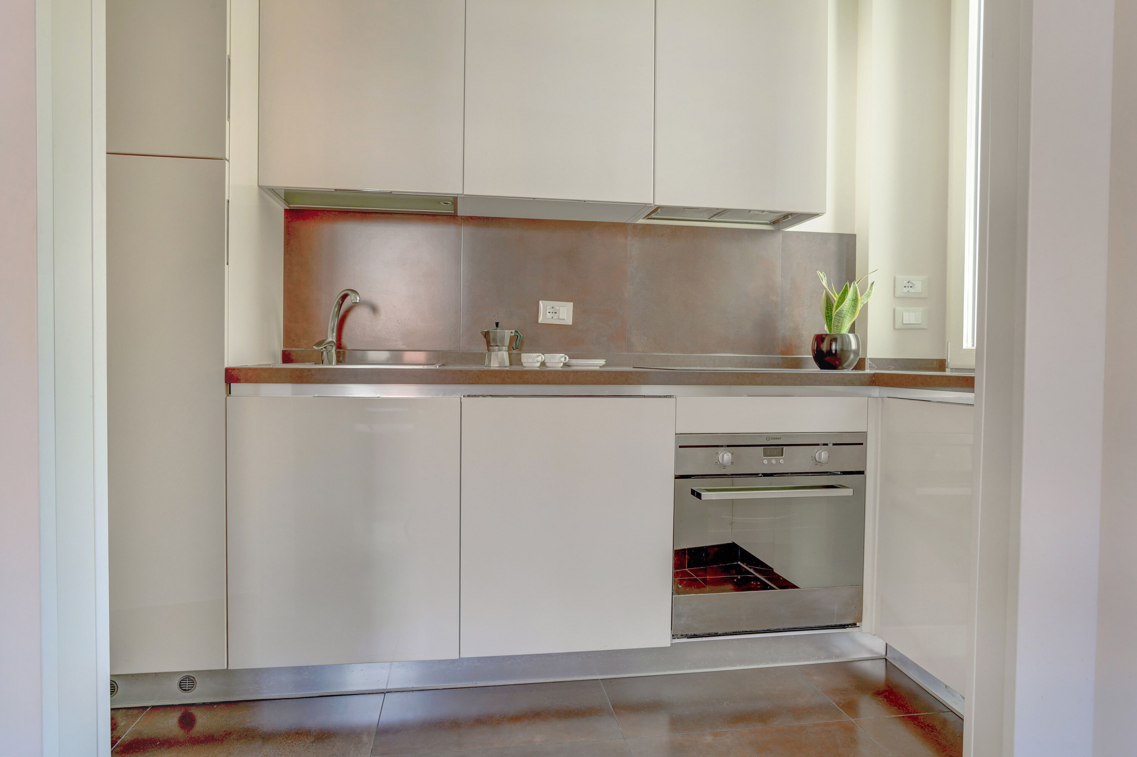 Una cocina moderna con armarios blancos, electrodomésticos de acero inoxidable y un ventanal que proporciona luz natural.