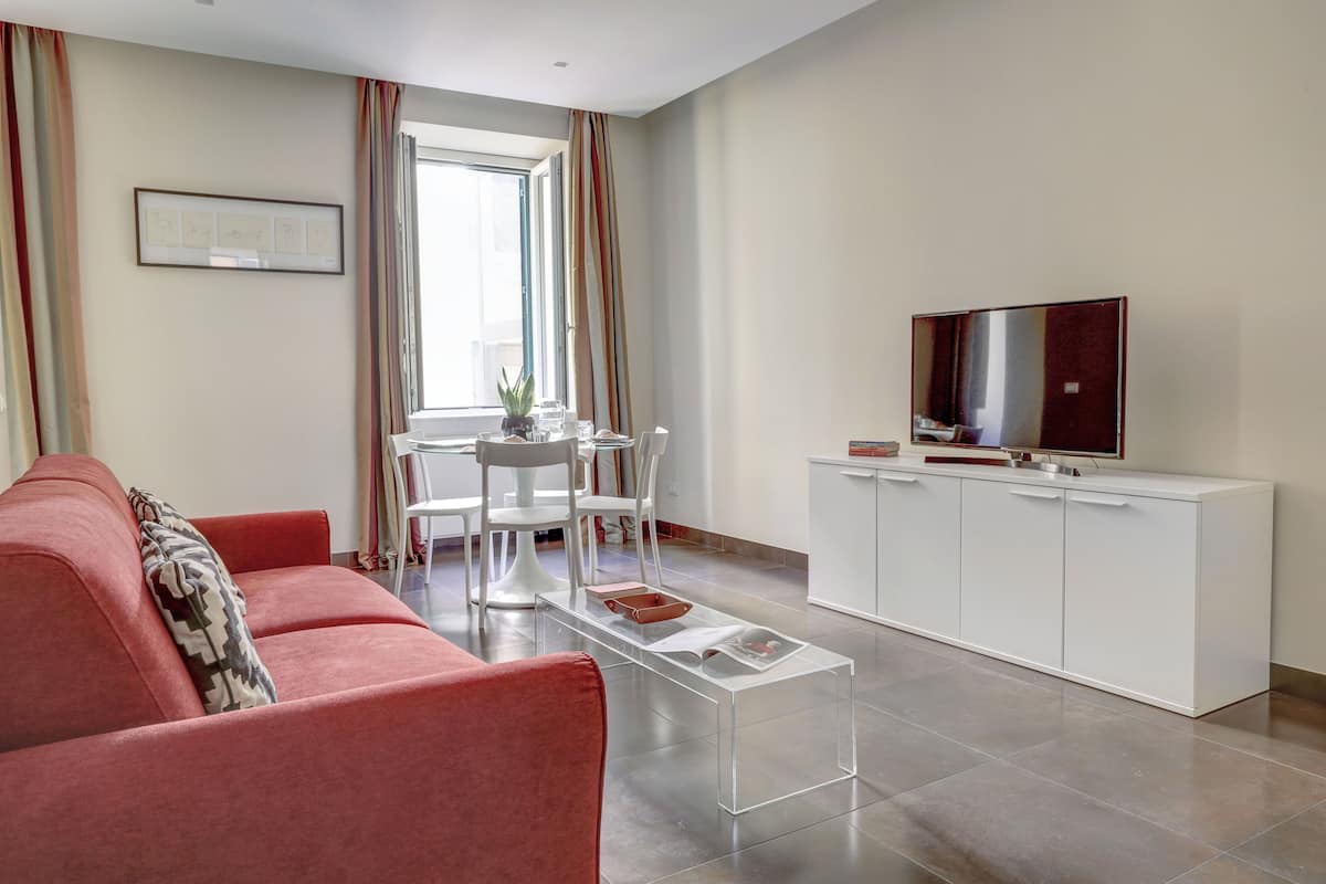 A modern living room with a red sofa, a white TV stand, and a clear coffee table.