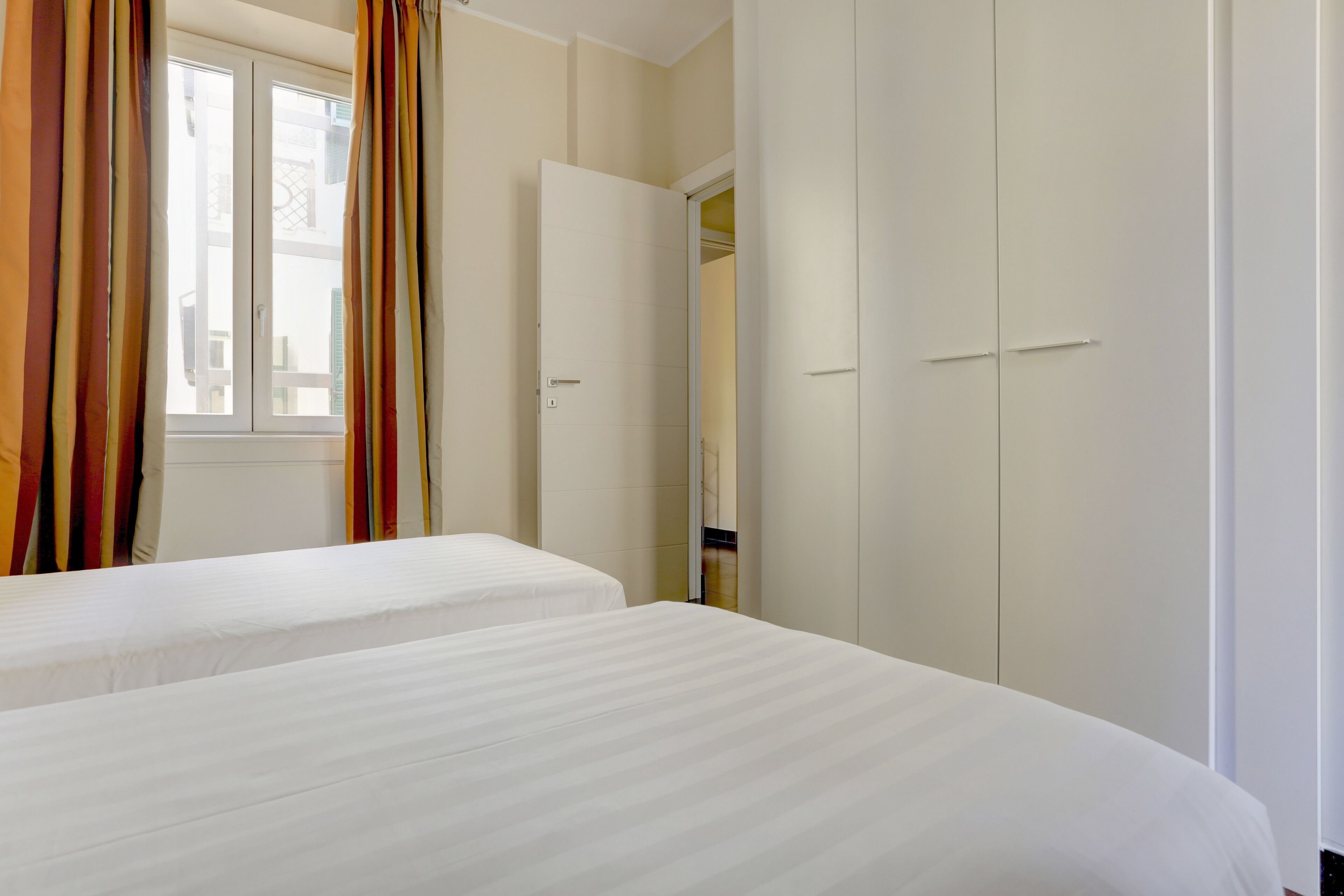 Una habitación de hotel con dos camas, un armario y una ventana con cortinas.