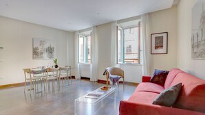 A spacious living room with a red sofa, a glass coffee table, and a dining area with a table and chairs. - Colosseo Gardens - My Extra Home (Rome)