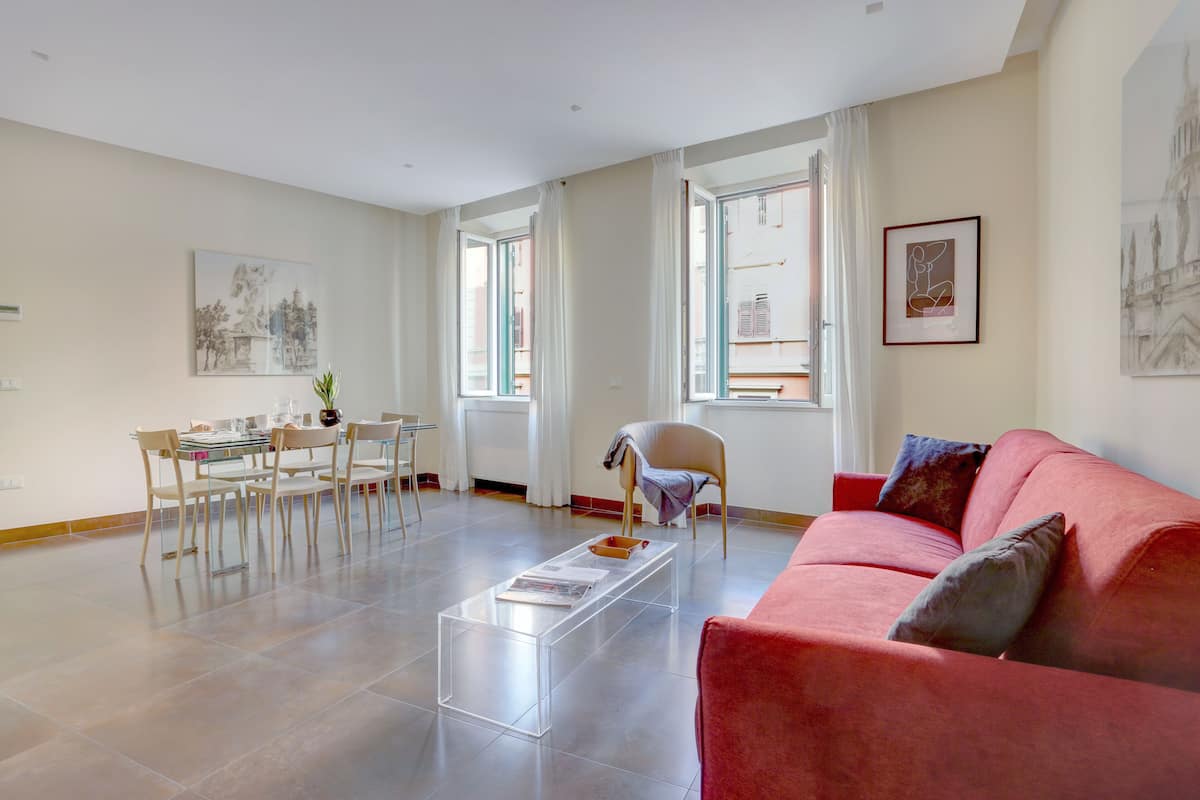 A spacious living room with a red sofa, a glass coffee table, and a dining area with a table and chairs.