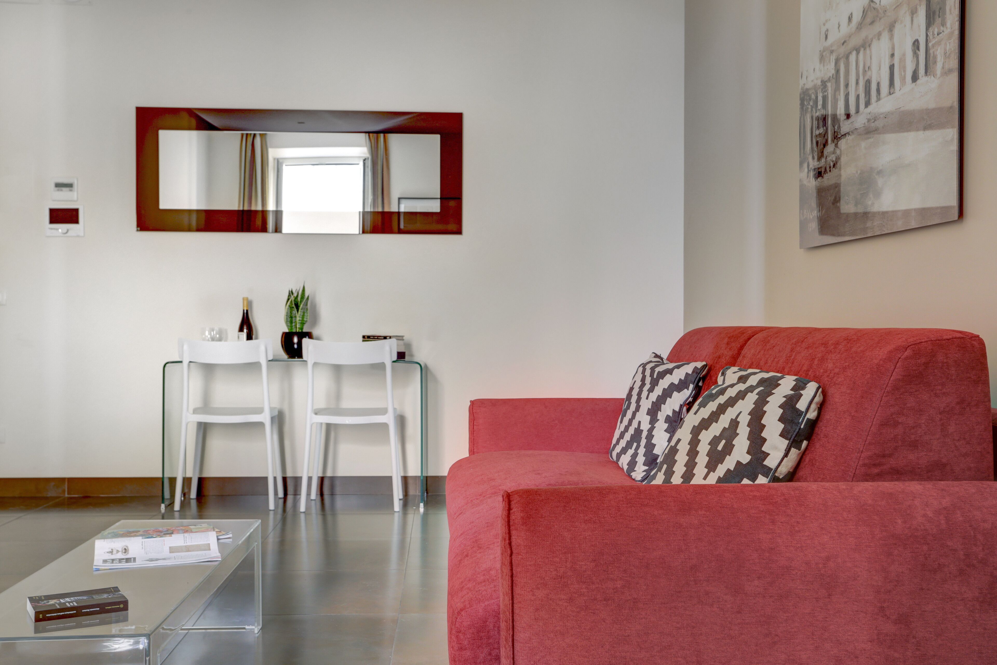 A modern living room with a red sofa, two white chairs, a glass coffee table, and a small side table with a plant.