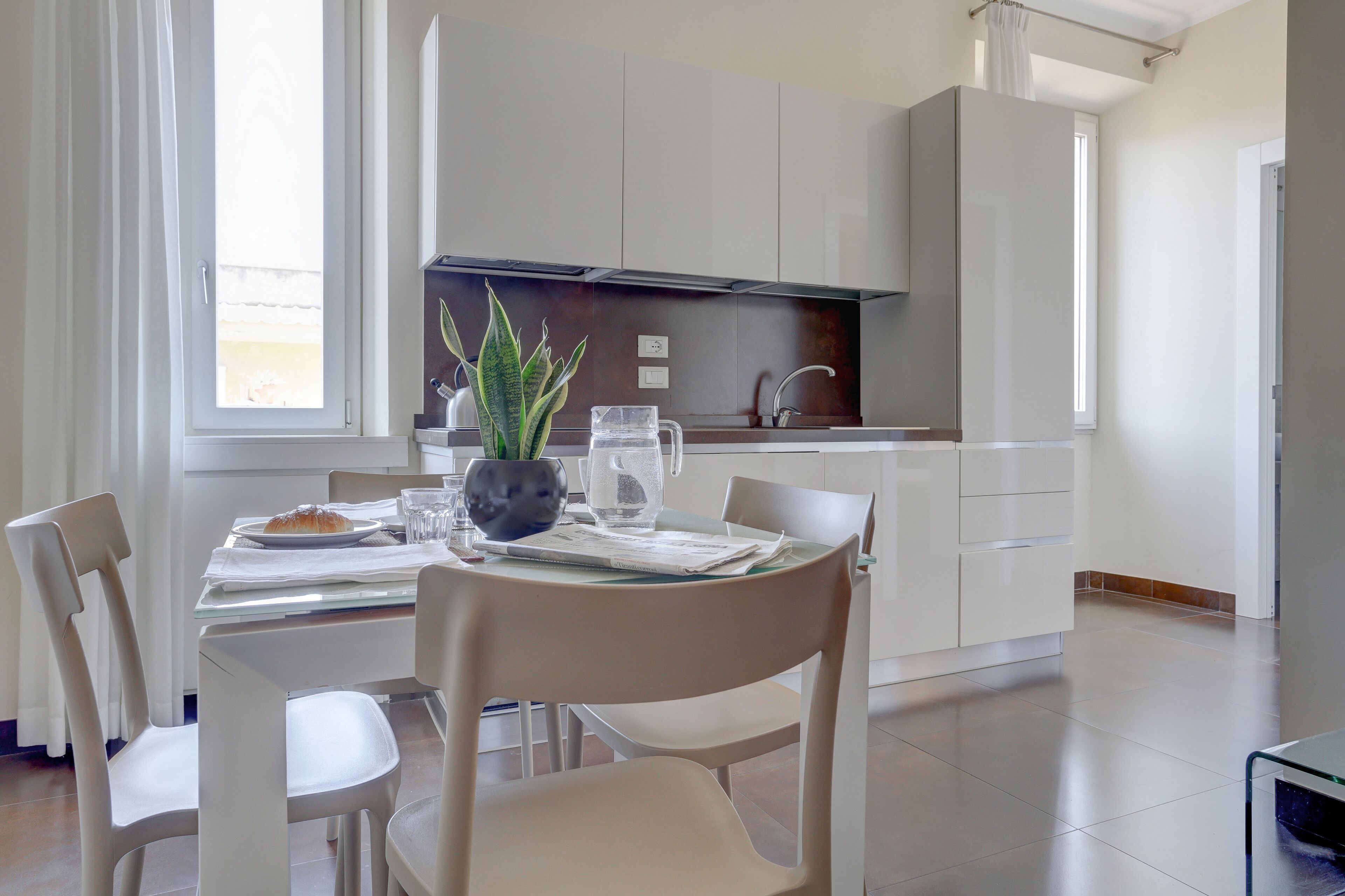 A modern kitchen with white cabinets, a dining table with chairs, and a potted plant.
