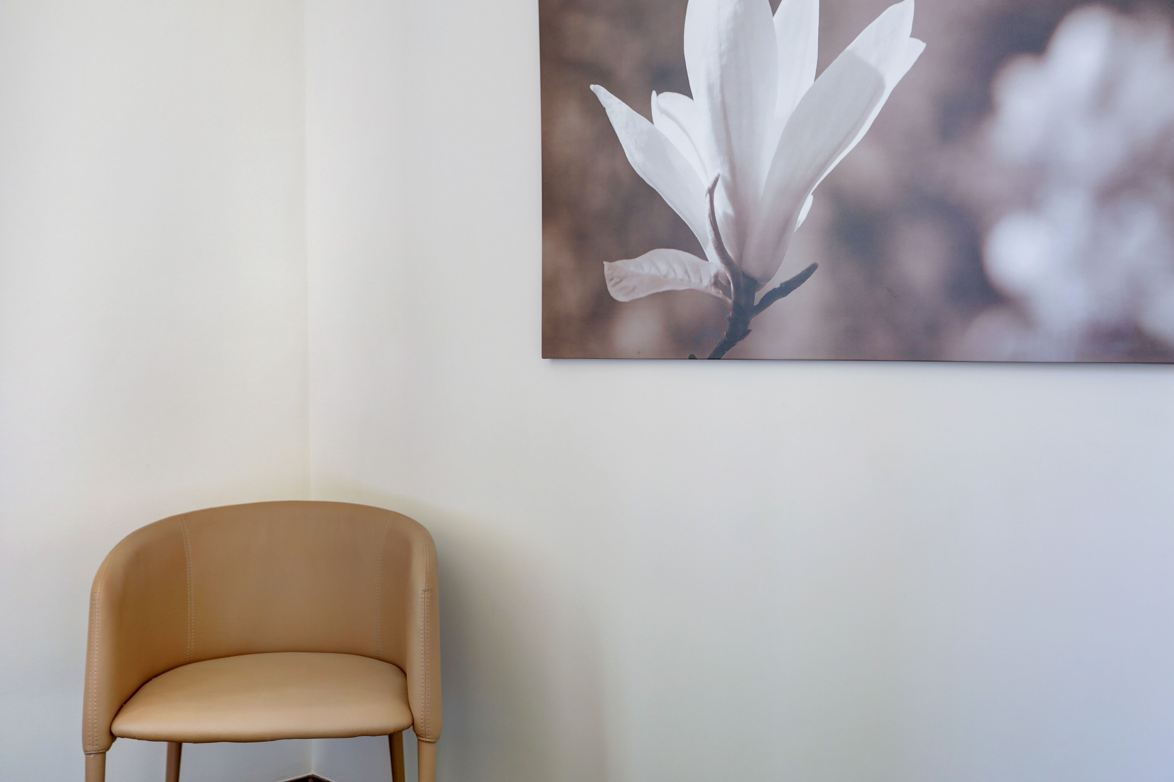 Una silla en una habitación con un cuadro de una flor de magnolia colgado en la pared.