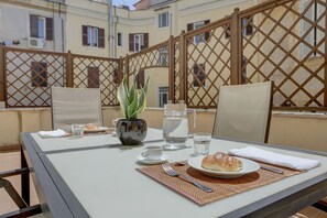 Een gedekte tafel voor twee met een croissant, een glas water, een kopje en een bloempot.