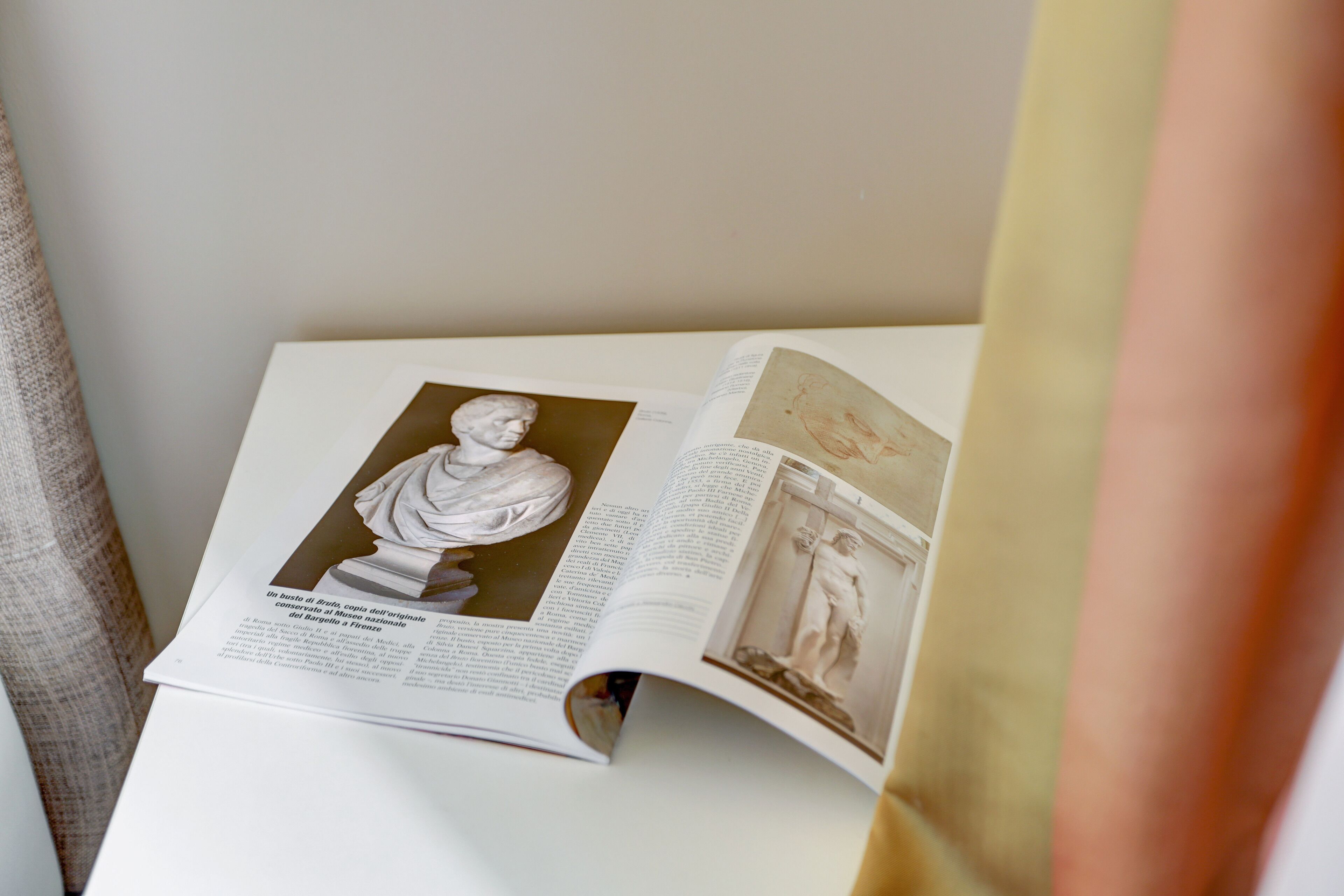 An open book with a marble bust and a photograph of a sculpture on a white surface.