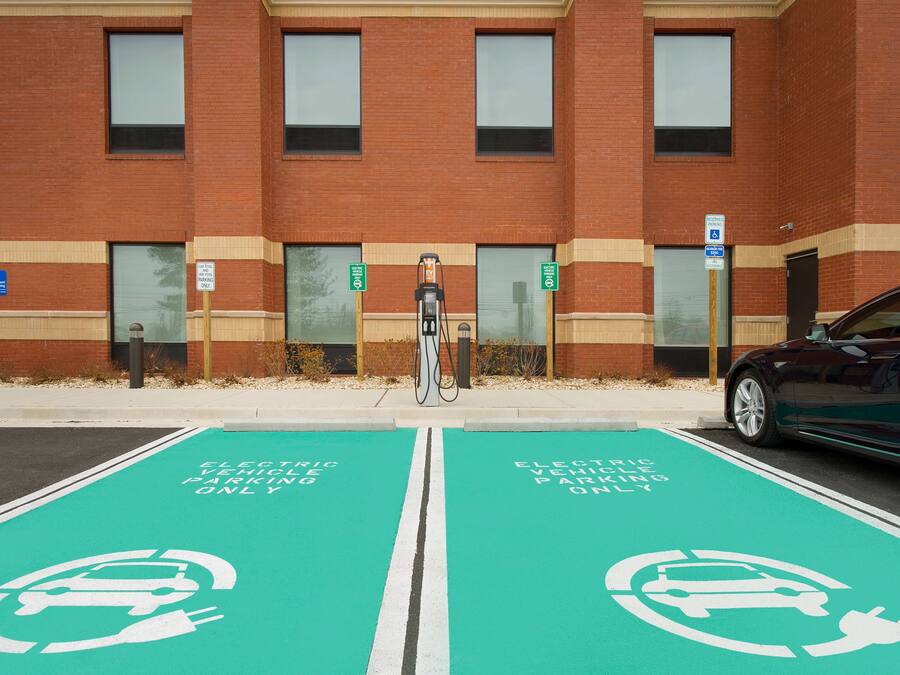 Un estacionamiento con estaciones de carga para vehículos eléctricos y un edificio de ladrillo al fondo.