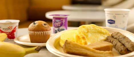 A plate with a muffin, a banana, a slice of cake, and two cups of yogurt.