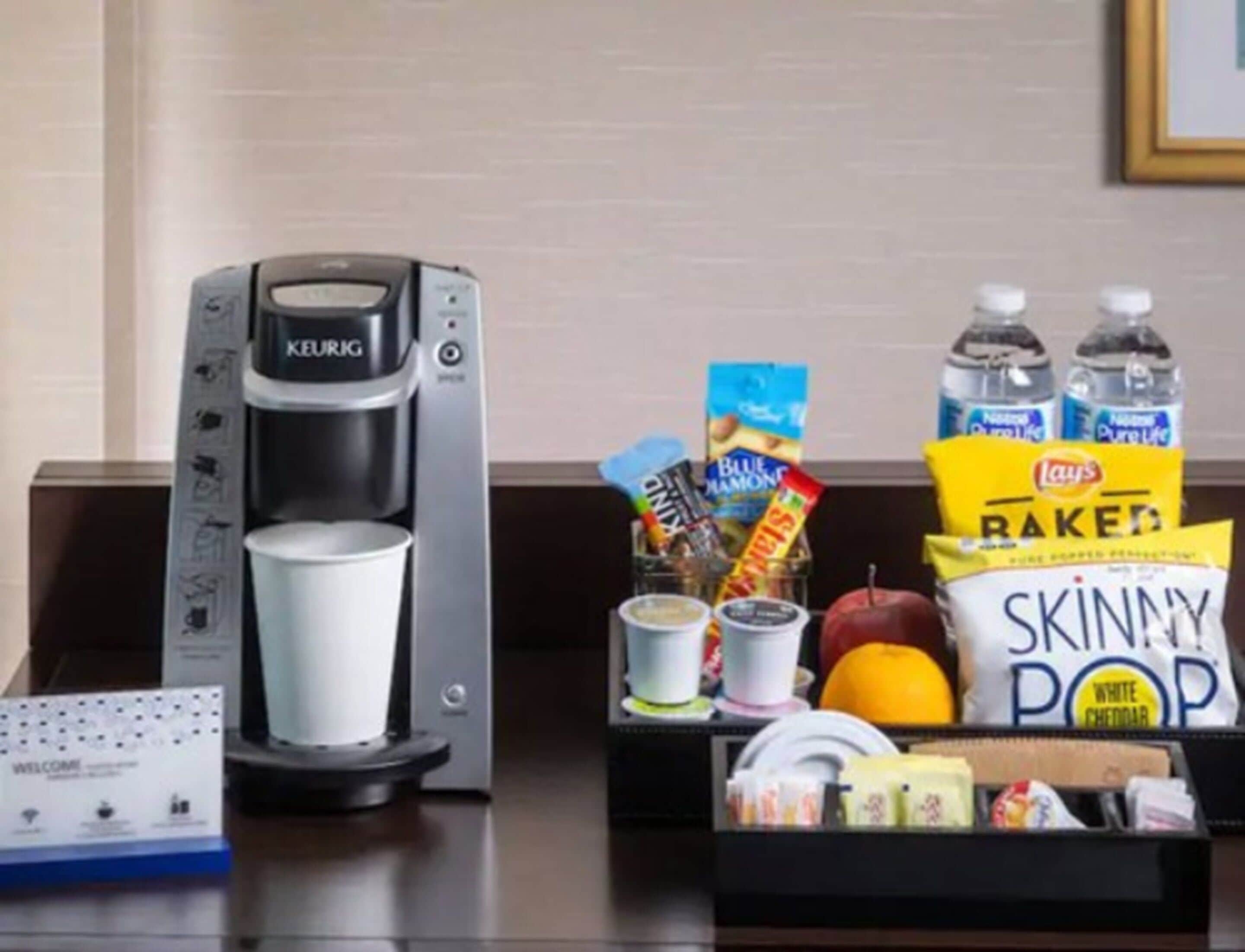 Una cafetera, una taza, aperitivos y agua embotellada sobre una mesa.