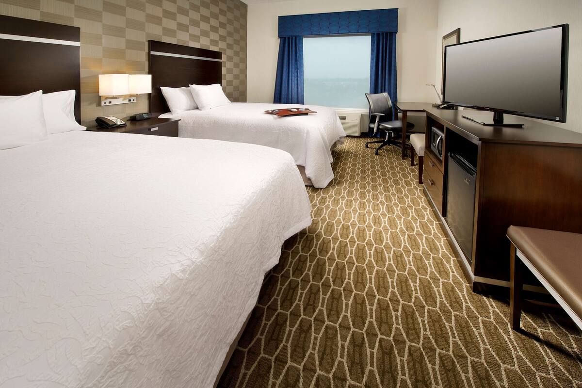 Ein Hotelzimmer mit zwei Betten, einem Schreibtisch mit Fernseher, einem Sessel und Meerblick.