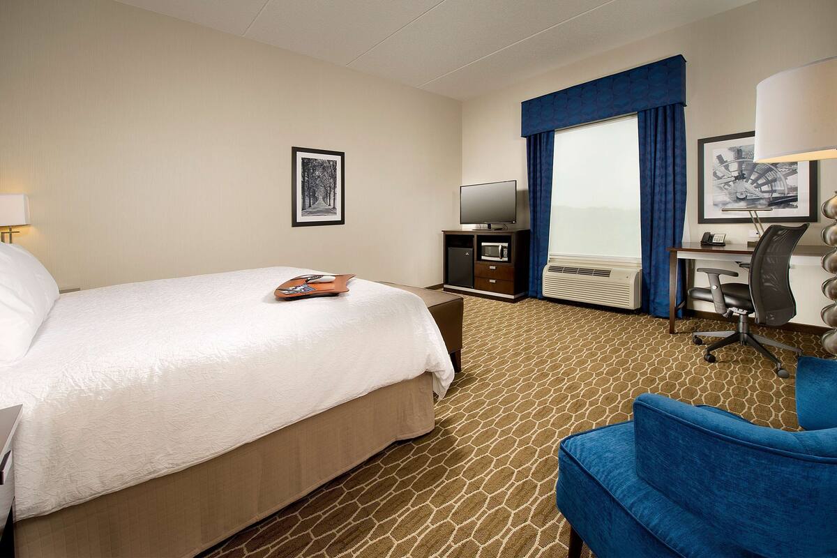 Ein Hotelzimmer mit einem Bett, einem Schreibtisch mit Computer, einem Fernseher und einem Sessel.