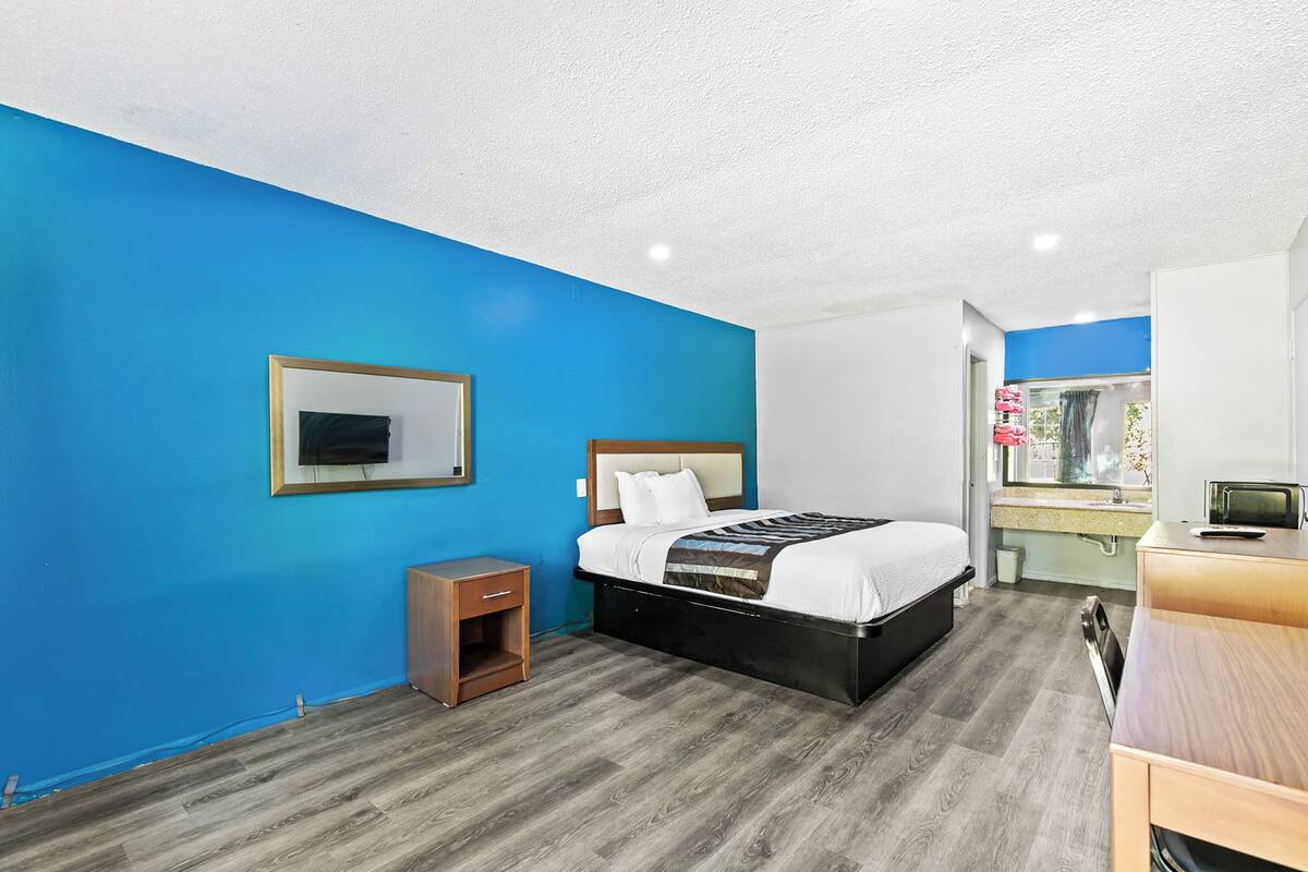 A hotel room with a bed, bedside table, and a desk with a chair.