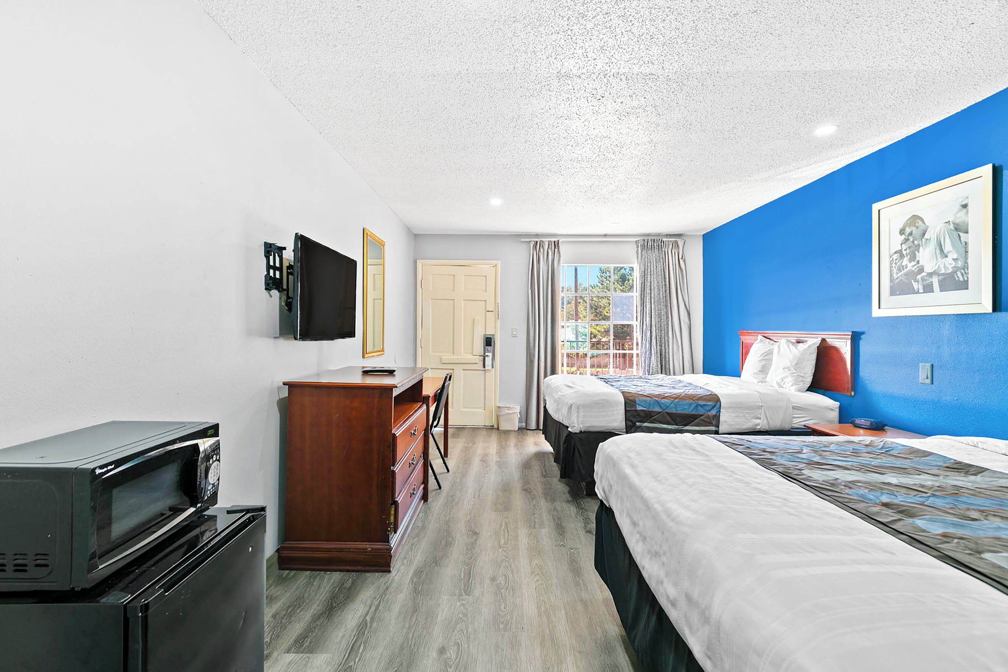 Habitació d'hotel amb dos llits, escriptori, televisió i finestra amb cortines.