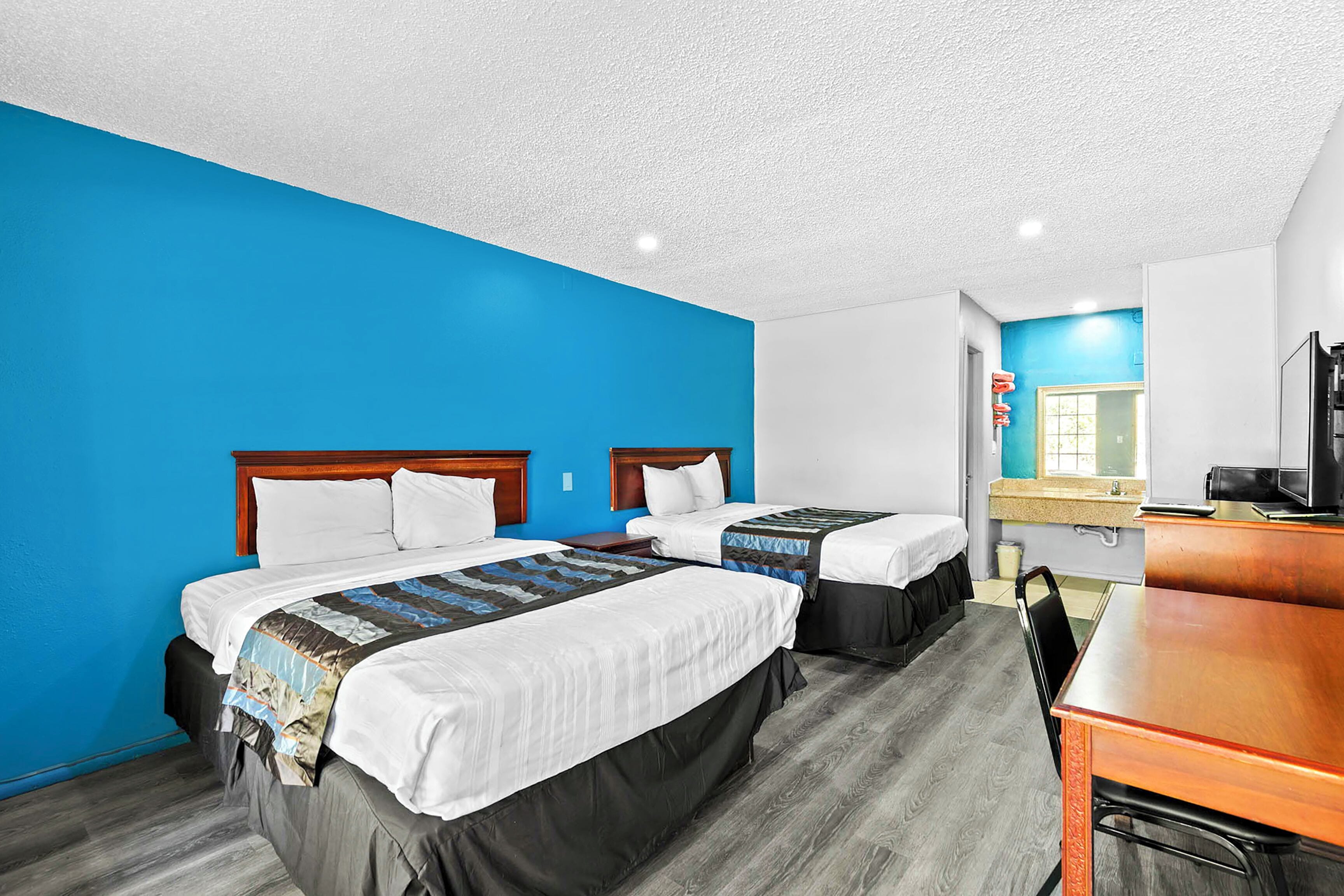 A hotel room with two beds, a desk, and a bathroom visible through an open door.