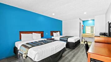 A hotel room with two beds, a desk, and a bathroom visible through an open door.