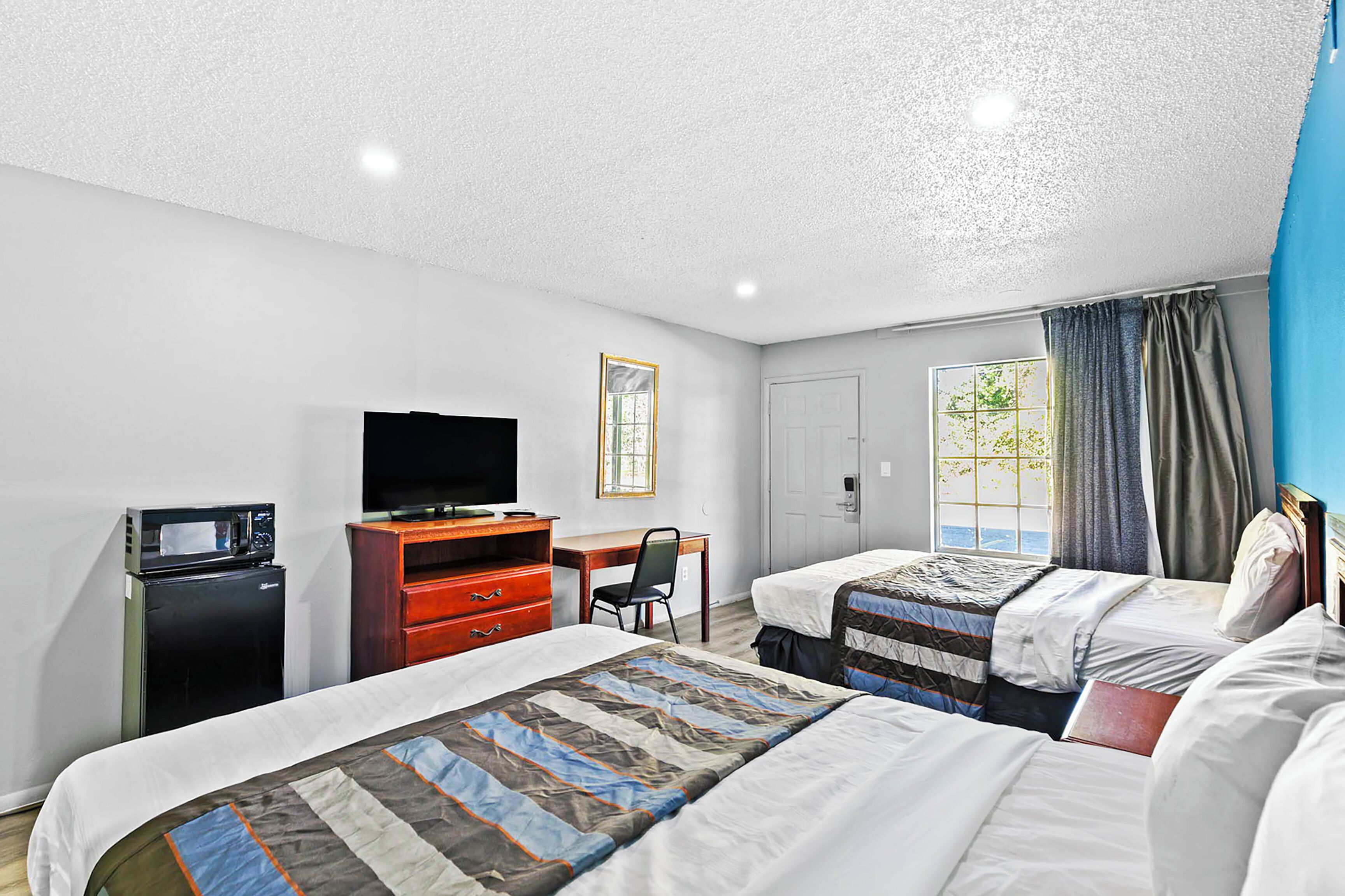 A hotel room with two beds, a desk, a television, and a small refrigerator.