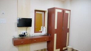 Une pièce comprenant une armoire en bois, un miroir, un téléviseur fixé au mur et une petite poubelle.