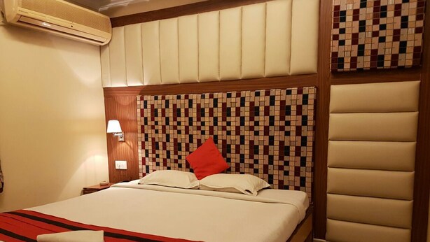 Une chambre d’hôtel avec un grand lit, une tête de lit ornée d’un motif en mosaïque, un oreiller rouge et un climatiseur fixé au mur.