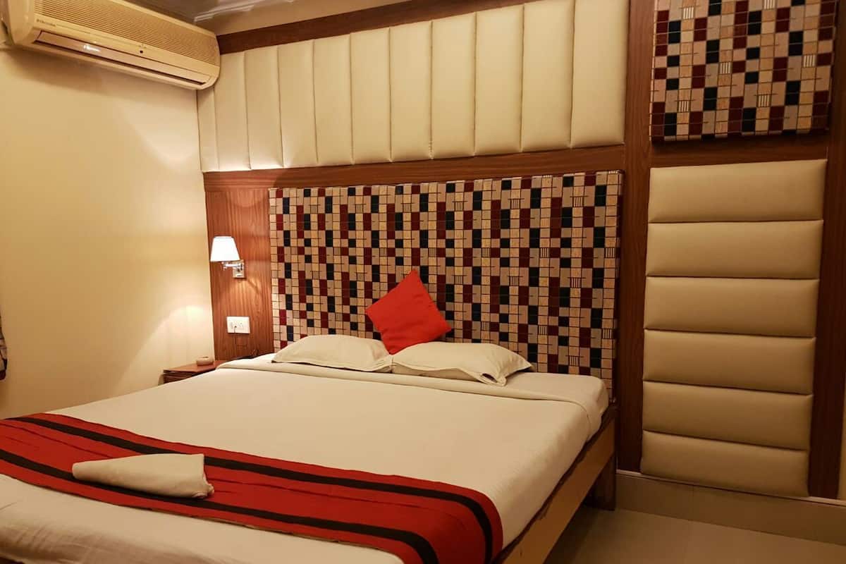 Habitació d'hotel amb un llit gran, un reposacapses amb dibuixos de mosaic, un coixí vermell i un aire condicionat fixat a la paret.