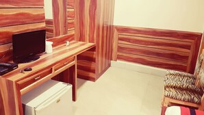 Une chambre de taille modeste, équipée d’un bureau en bois, d’une télévision, d’un petit réfrigérateur et d’un fauteuil à motifs de rayures de tigre.