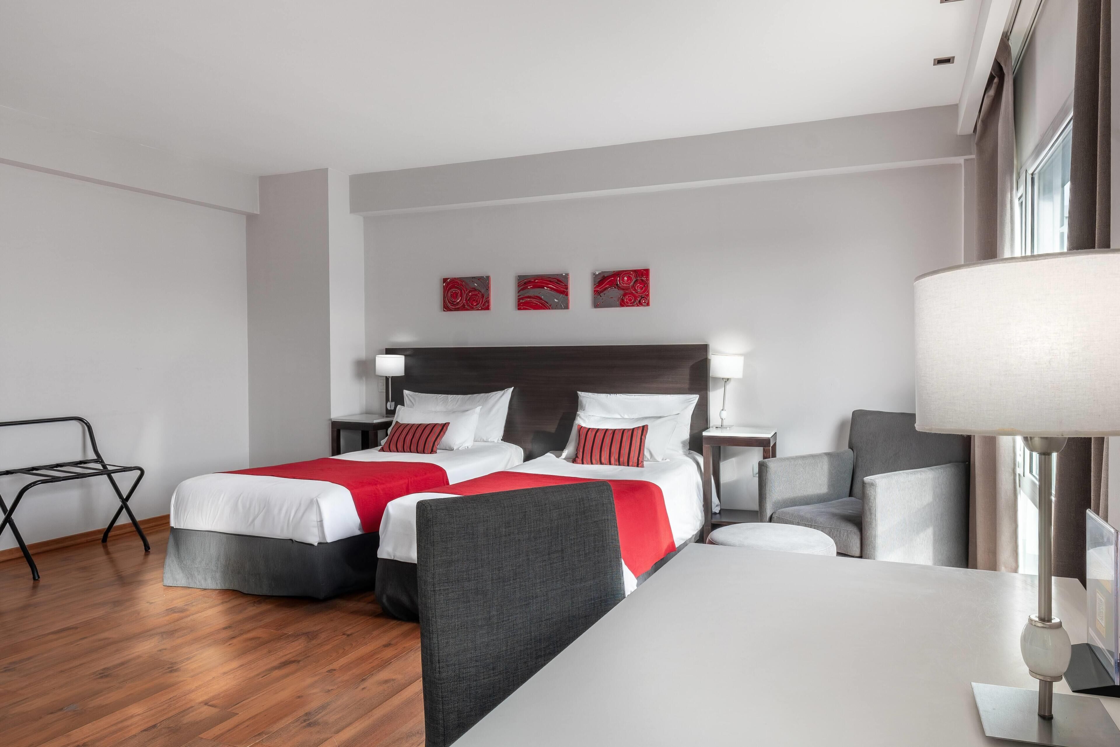 A hotel room with two beds, a desk, a chair, and a lamp.