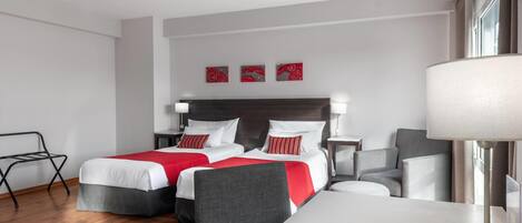 A hotel room with two beds, a desk, a chair, and a lamp.