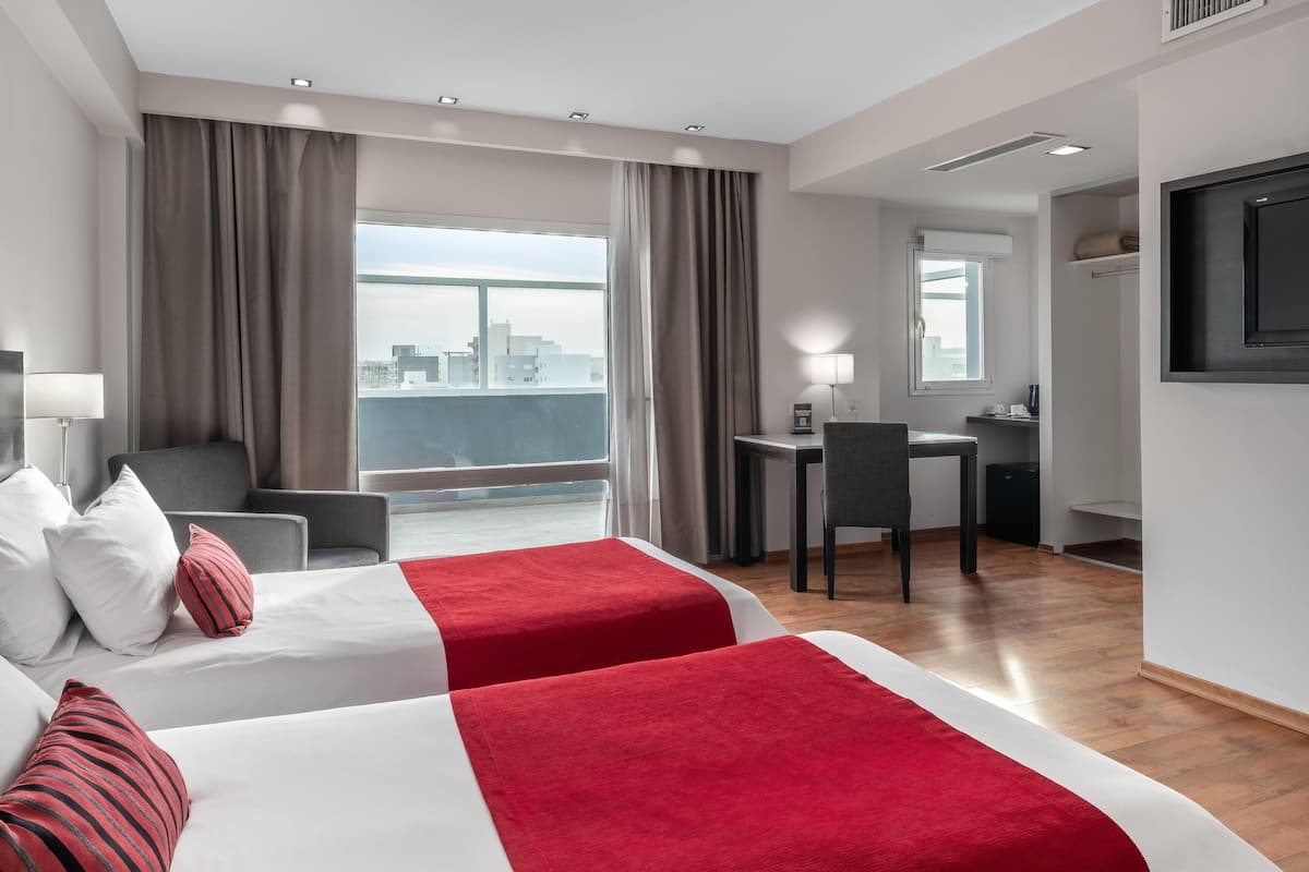 A hotel room with two beds, a desk, a chair, a TV, and a city view.