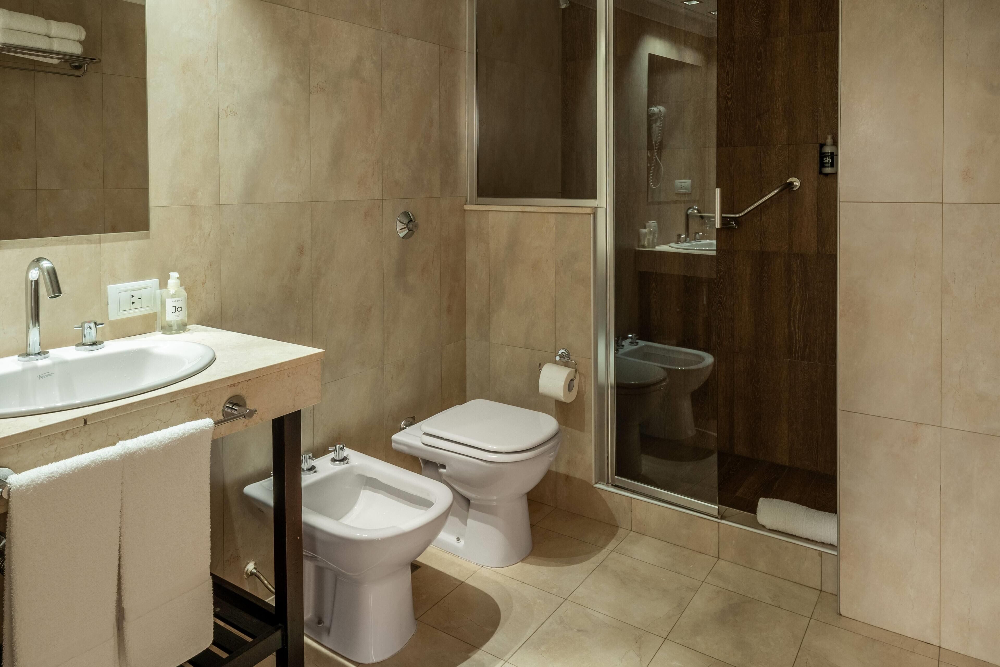 Et moderne badeværelse med vask, bidet, toilet og brusekabine i glas.