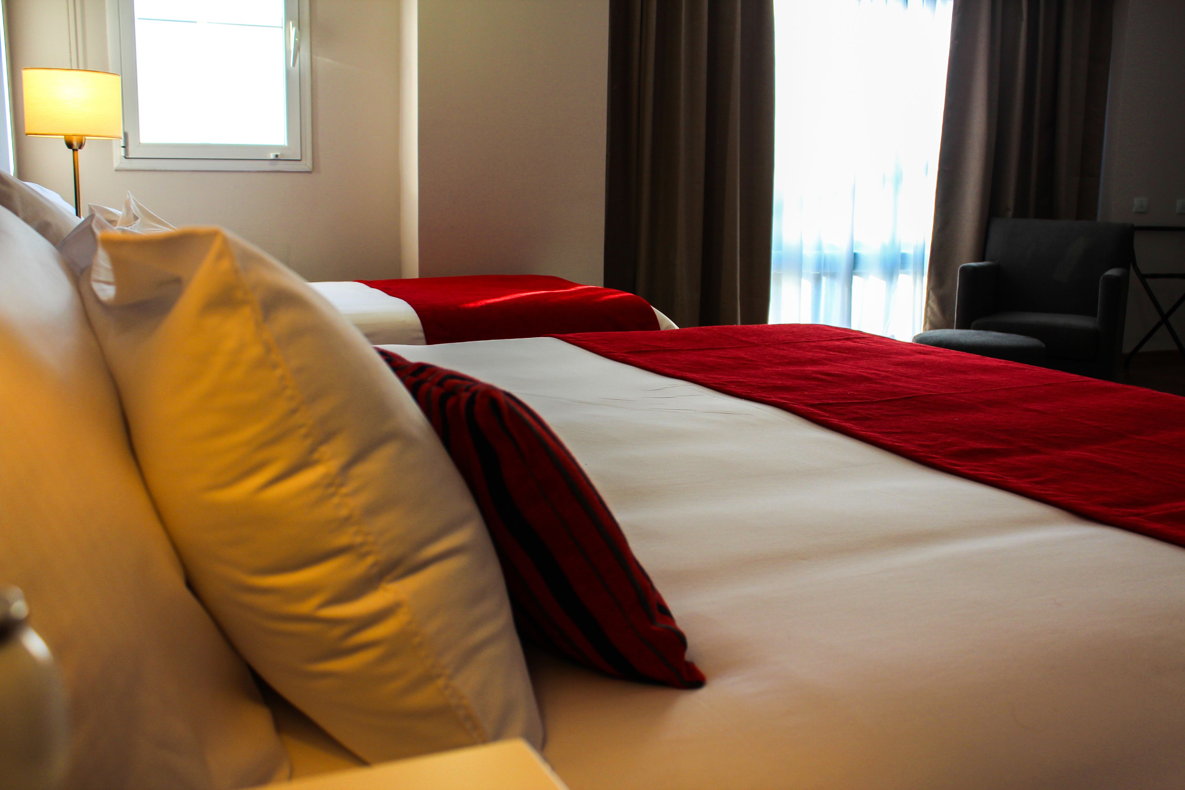 A hotel room with two beds, a lamp, a chair, and a view of the outdoors.