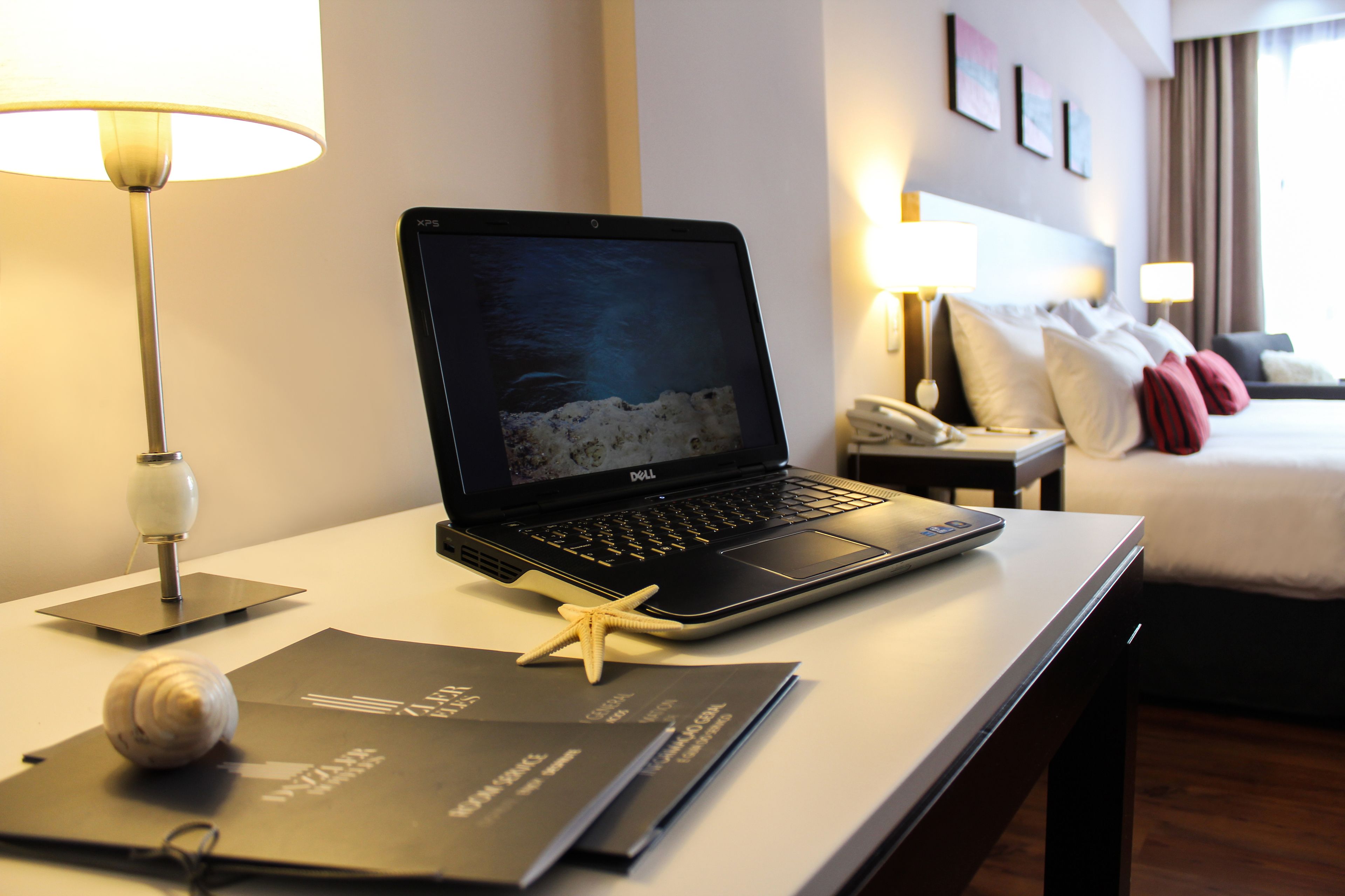 Una habitación de hotel con una computadora portátil sobre un escritorio, una decoración de estrella de mar y una cama con almohadas.