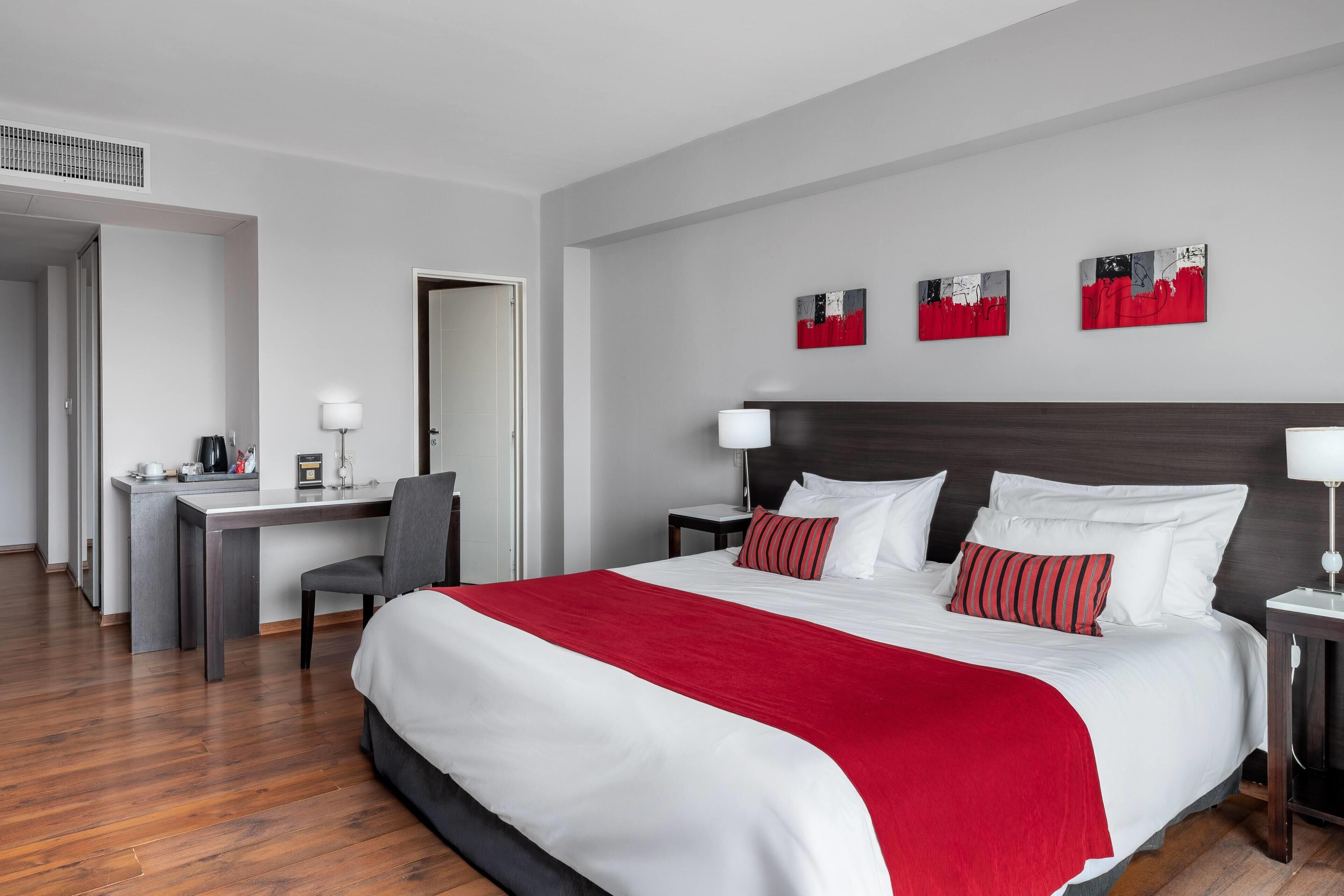 Habitación de hotel con una cama grande, un escritorio y una silla. Hay tres cuadros en la pared.