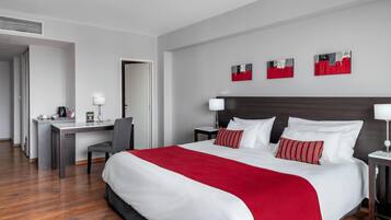 Habitación de hotel con una cama grande, un escritorio y una silla. Hay tres cuadros en la pared.