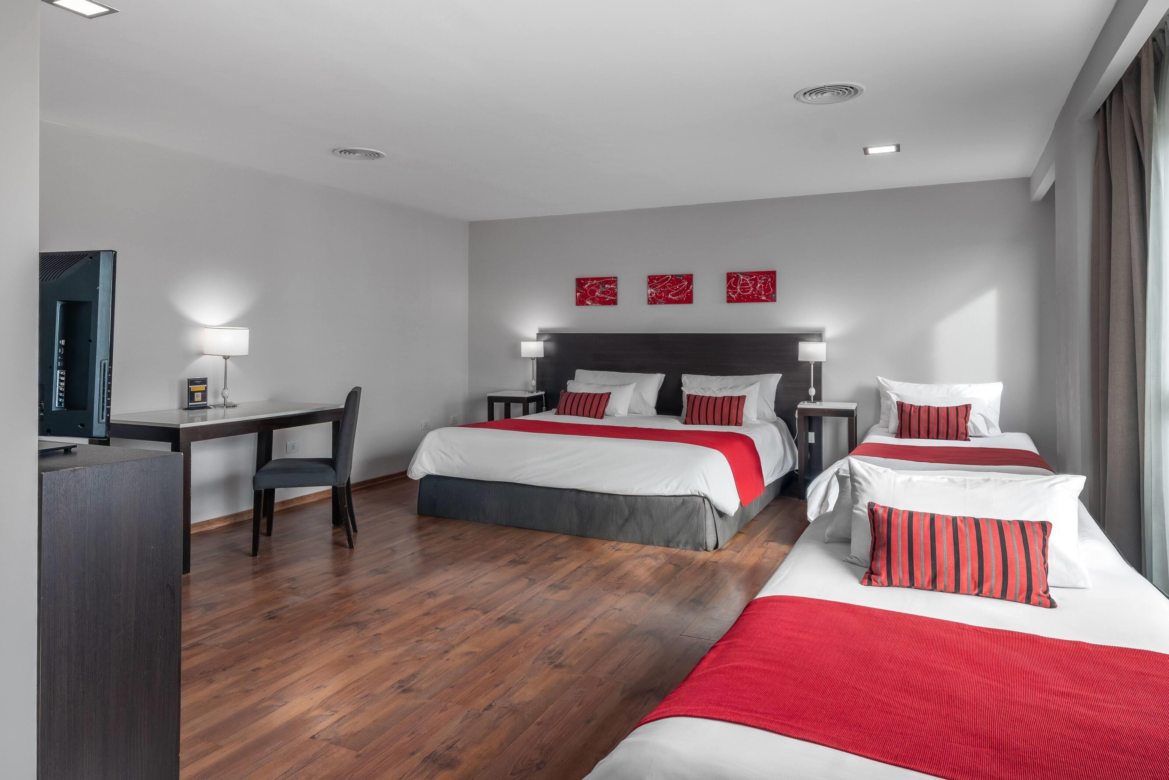 A hotel room with two beds, a desk, and a TV.