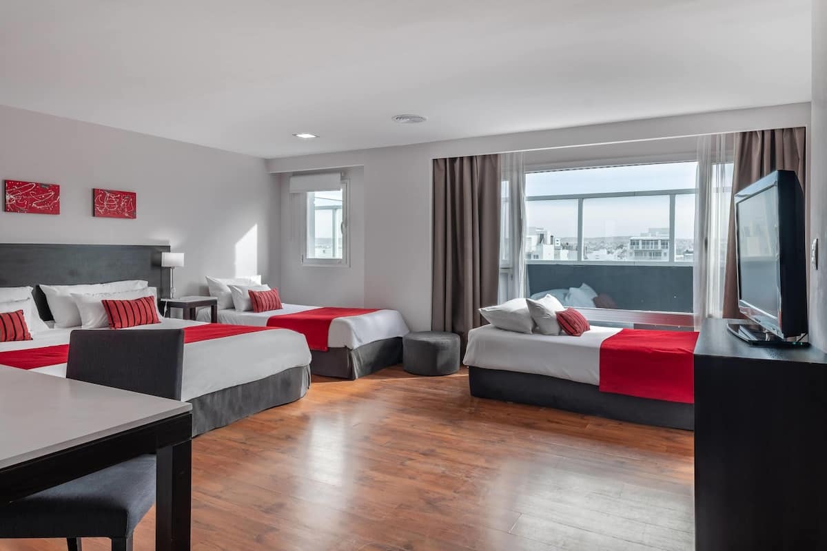 A hotel room with two beds, a TV, a dining table, and a city view.