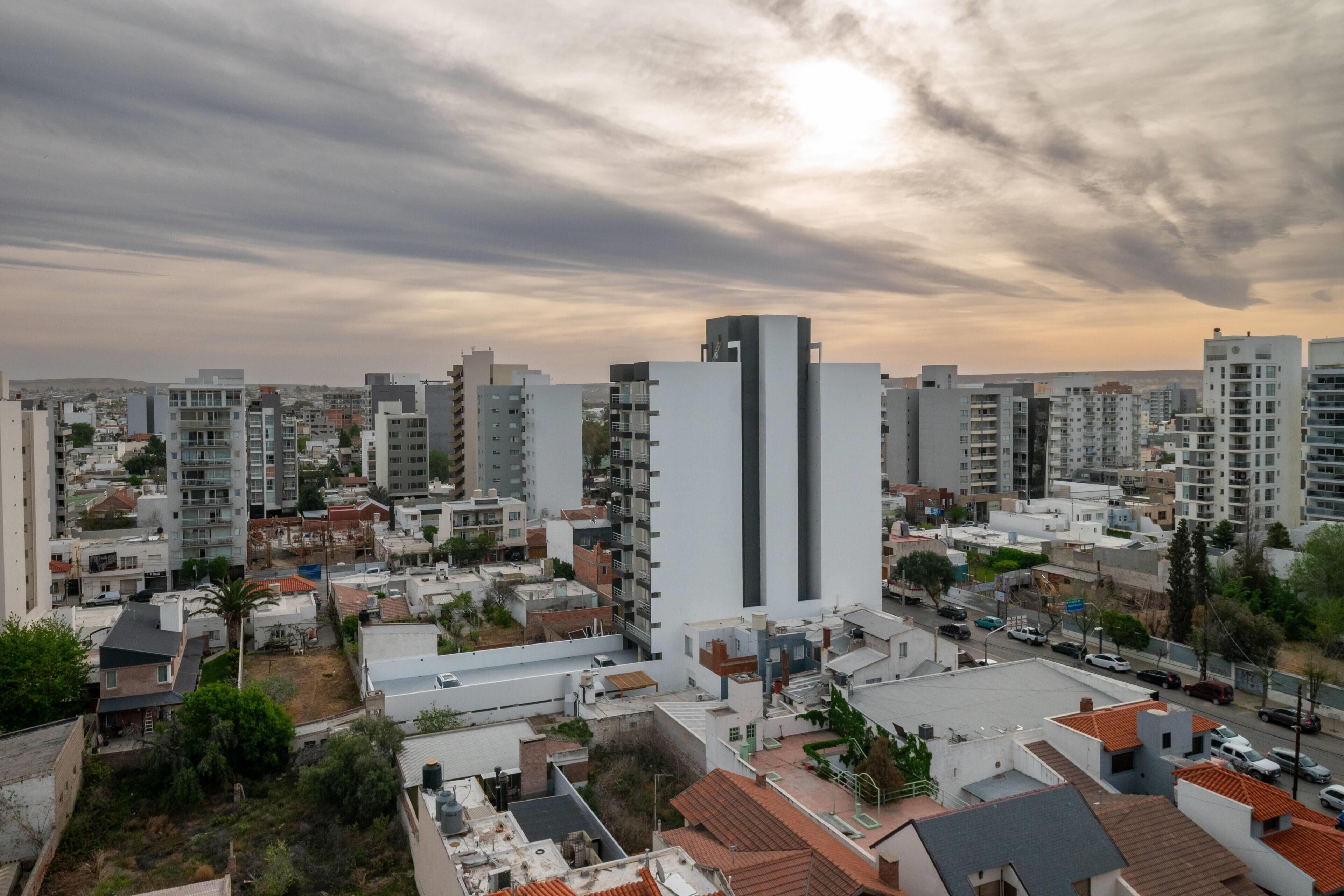 Un paisaje urbano con edificios modernos, un rascacielos blanco destacado y un cielo despejado.