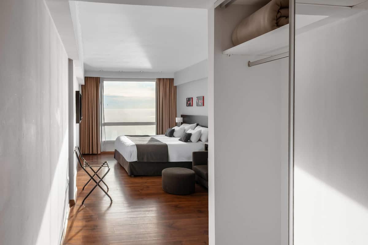 A modern hotel room with a large bed, a seating area, and a view of the sky.