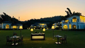 A well-lit outdoor dining area with tables and chairs, surrounded by a large, multi-story building with arched windows and balconies. - The Hridayesh SPA Wilderness Resort (Ramnagar)