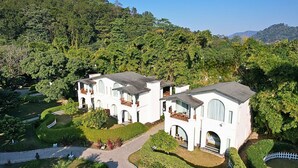 A large, white, multi-story building with arched windows and balconies, surrounded by lush greenery and a well-maintained garden. - The Hridayesh SPA Wilderness Resort (Ramnagar)