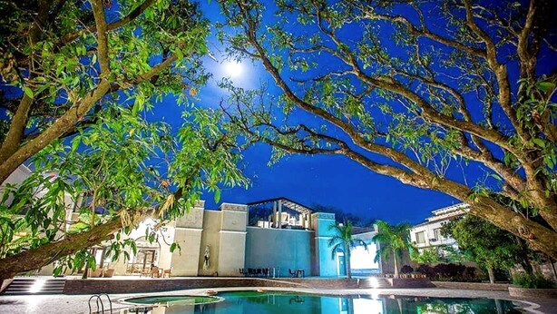 A nighttime view of a pool area with a clear sky, surrounded by trees and buildings. - The Hridayesh SPA Wilderness Resort (Ramnagar)