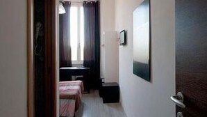A narrow hallway with a bed, a desk, and a mirror on the wall. - MF Hotel (Rome)