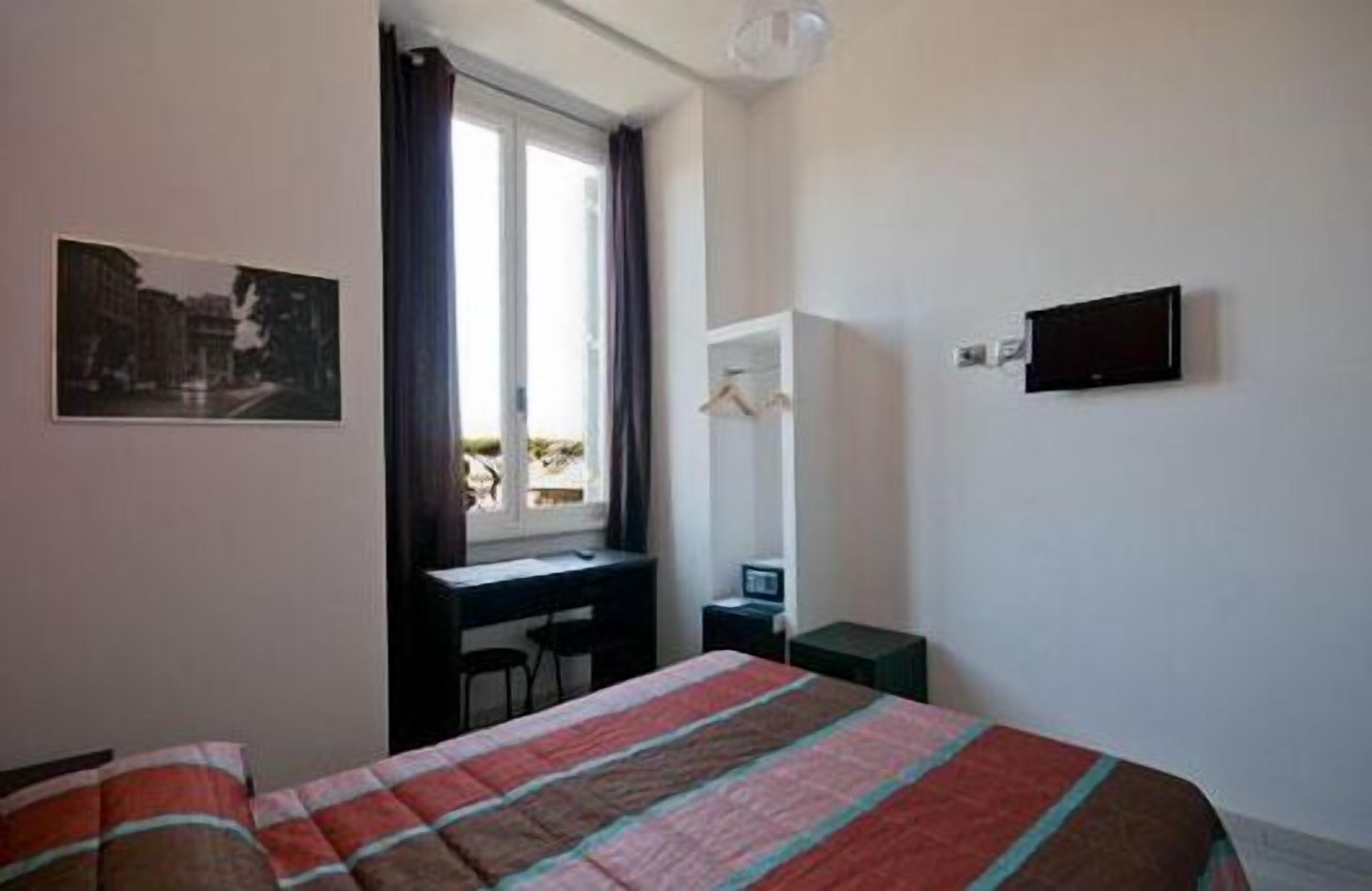 A hotel room with a bed, a desk, a chair, a television, and a window with curtains.