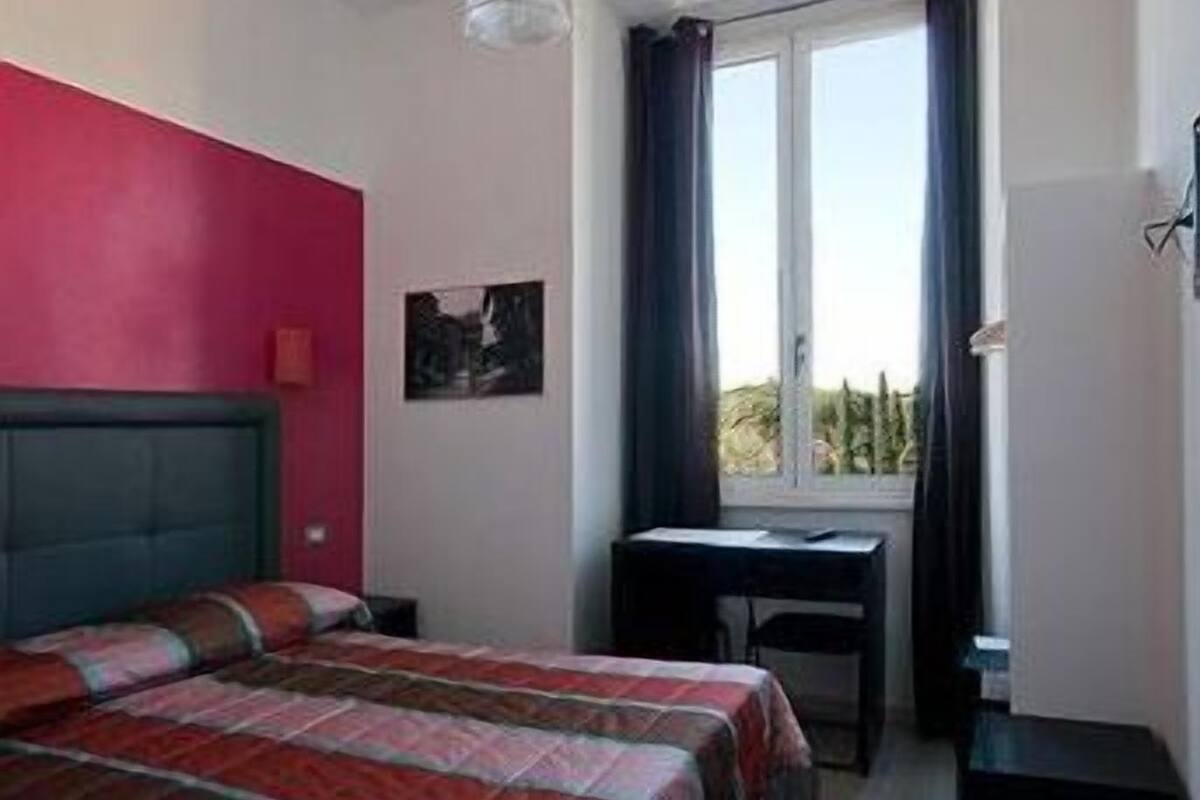 Un dormitorio con cama, escritorio, ventana con cortinas y lámpara de pared.