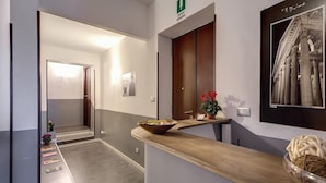 A hotel reception area with a wooden counter, a mirror, a framed picture, and a potted plant. - MF Hotel (Rome)