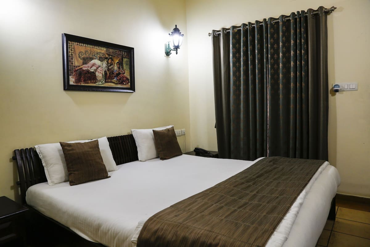 A neatly made bed with a brown blanket, a wall-mounted light, and a framed picture above it.
